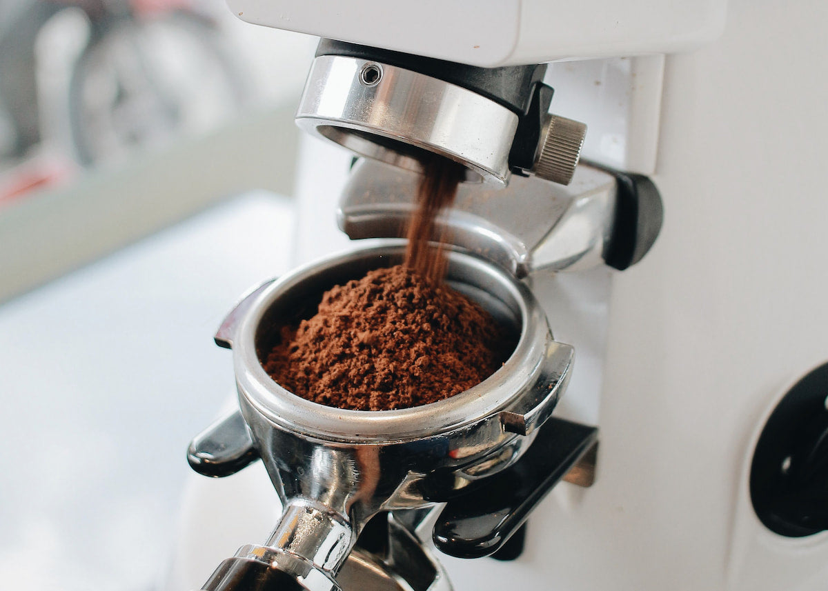 Commercial espresso grinder dispensing freshly ground coffee into a portafilter before espresso extraction in a specialty café.